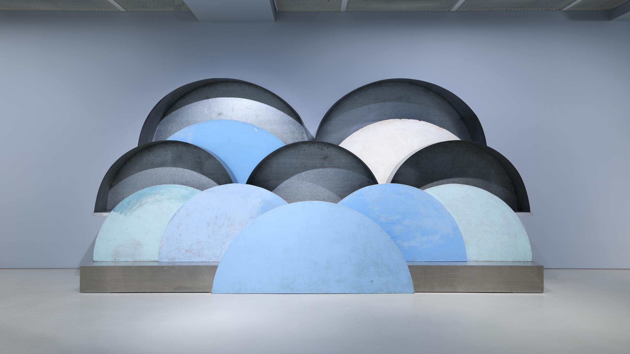 전시장 벽 앞에 파랑·회색 계열의 반원형 구조물들이 층층이 겹쳐 설치된 추상 조형 작품