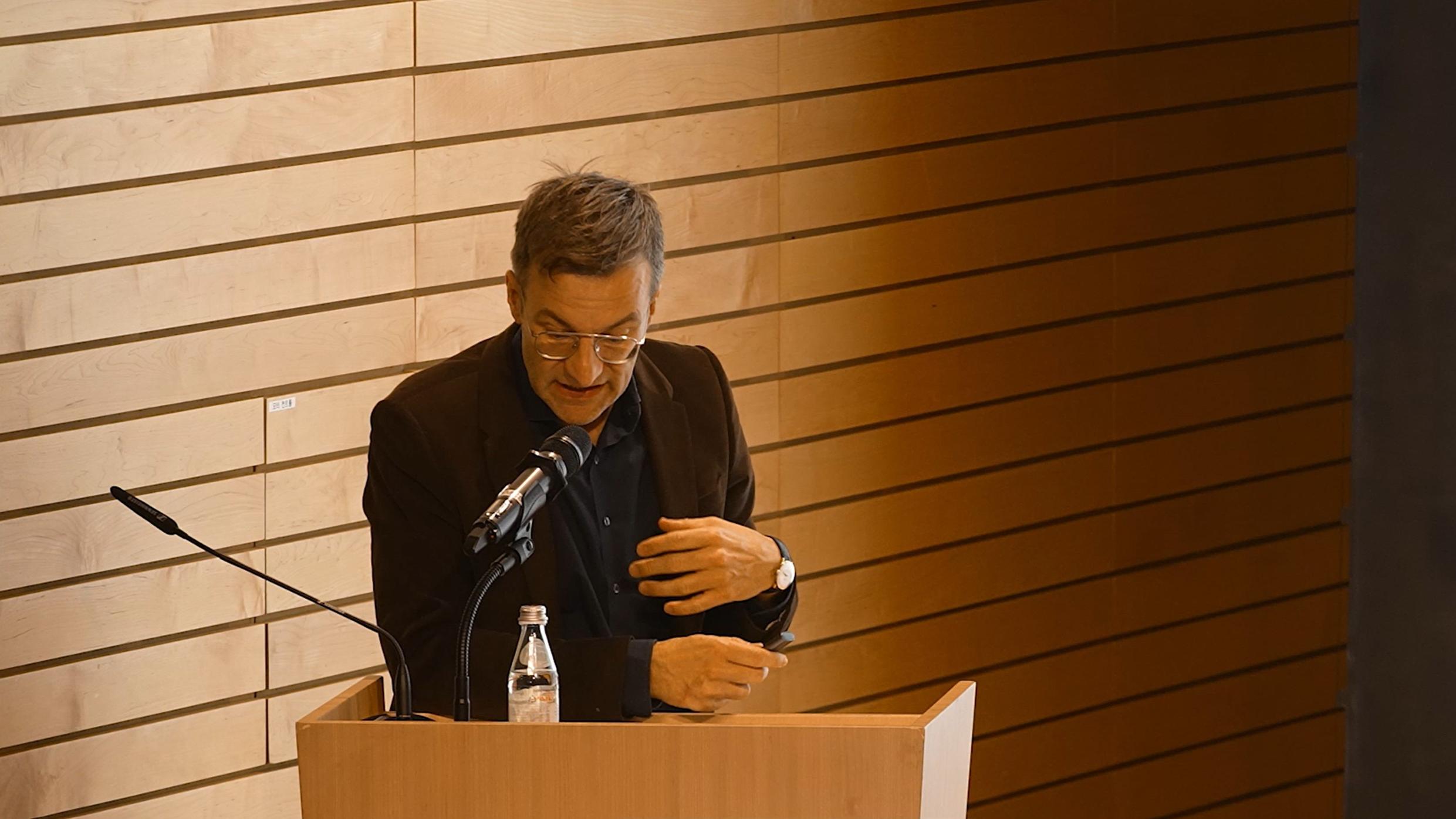 강연장에서 연단에 서서 마이크로 발표하는 모습